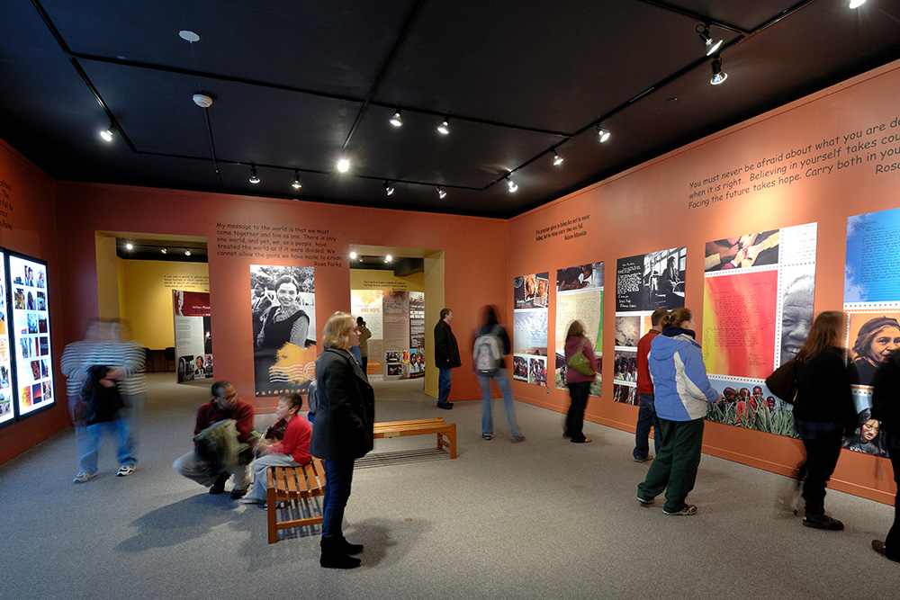 Interior of a museum with people looking at large colorful posters