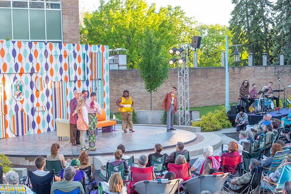 Outdoor 1960's style theatre performance in front of a seated crowd